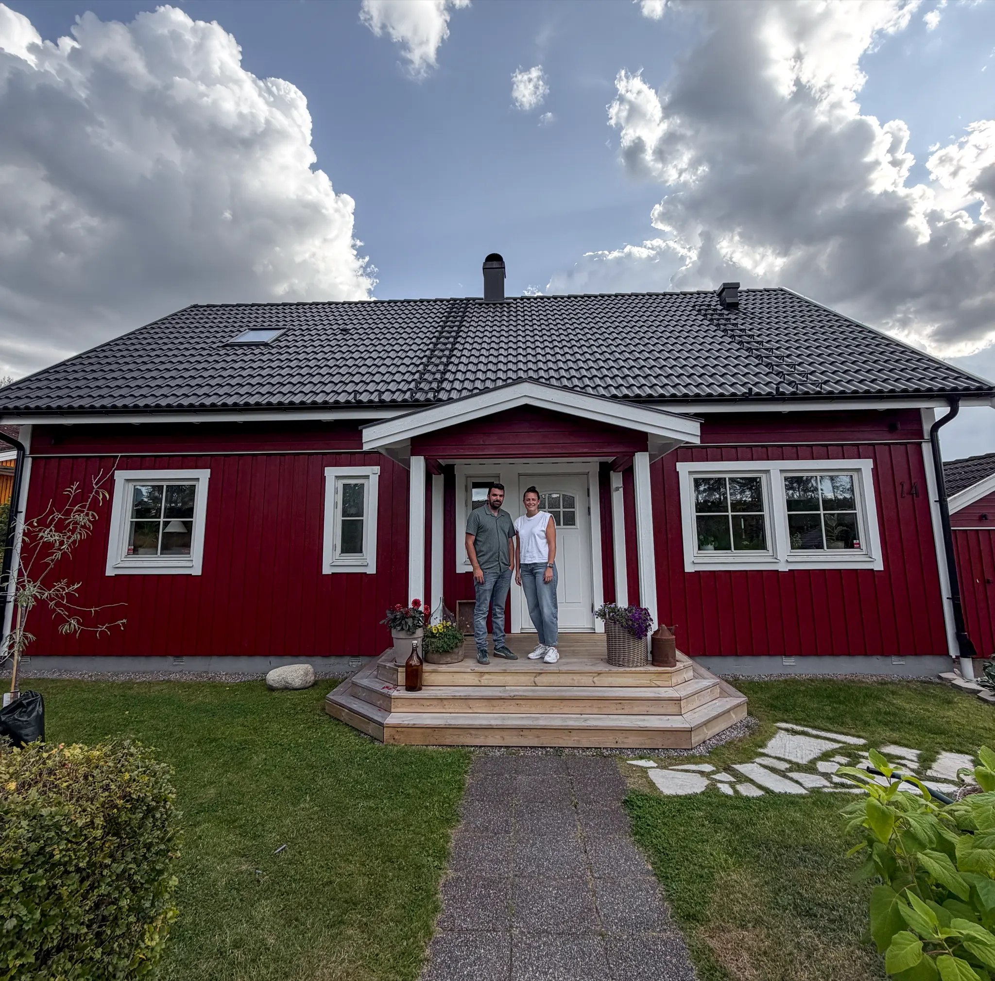 Ett par på trappan till sin röda villa med nytt tegeltak